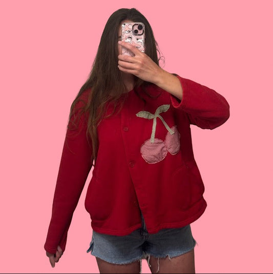 Person wearing a red sweater with cherry design against a pink background