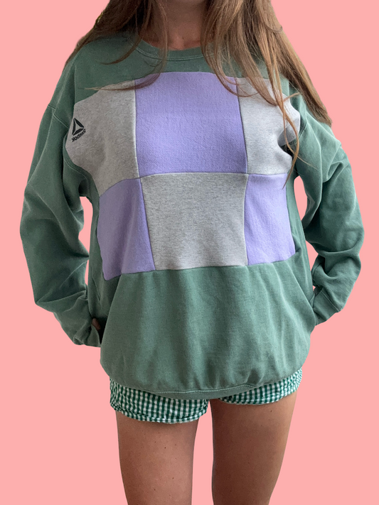 Green patchwork sweatshirt worn by a person on a pink background